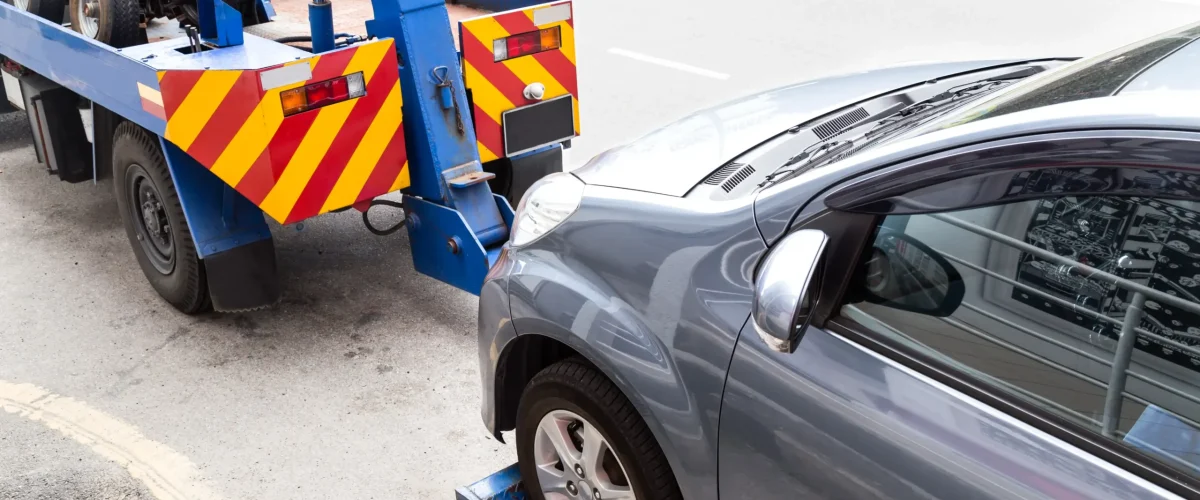 A tow truck towing a broken car on the street.