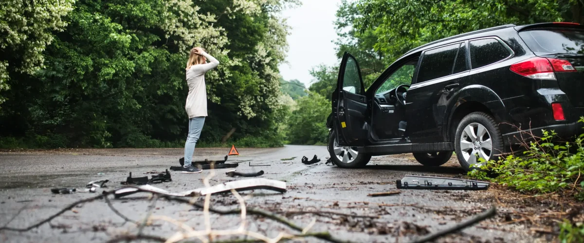 A young woman standing by the damaged car after an accident.